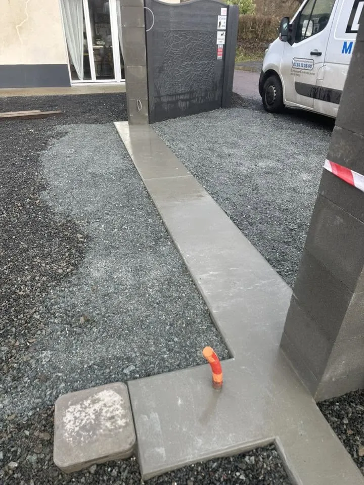 Bordure béton coulée délimitant une allée gravillonnée, avec piliers de portail en blocs