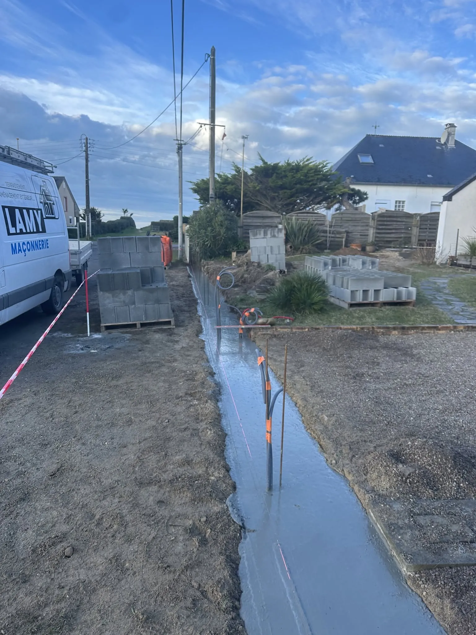Coulage d'une semelle de fondation en béton pour un mur de clôture, blocs à bancher stockés à côté