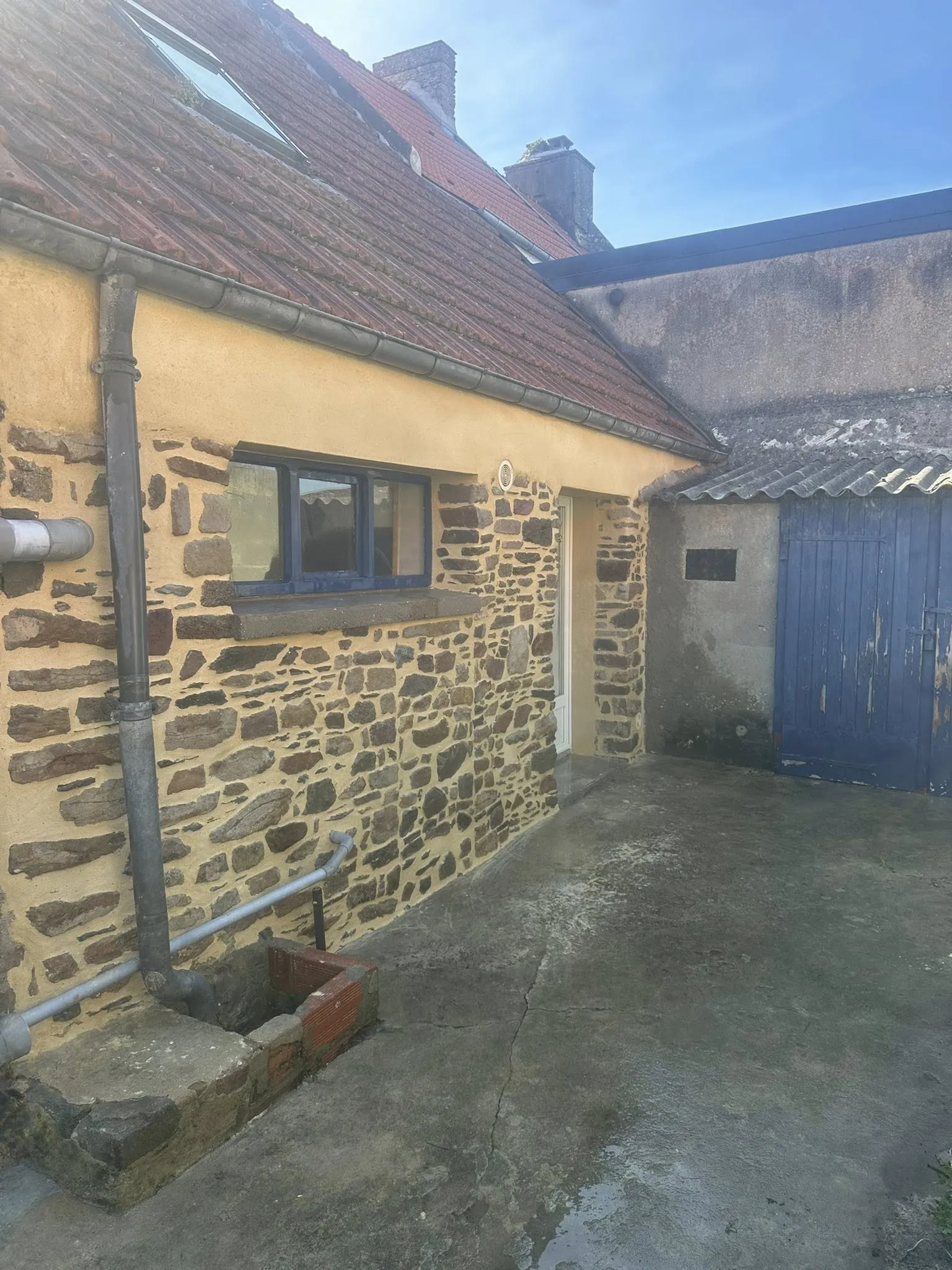 Façade de maison ancienne mêlant pierre apparente et enduit à la chaux teinté, avec cour en béton
